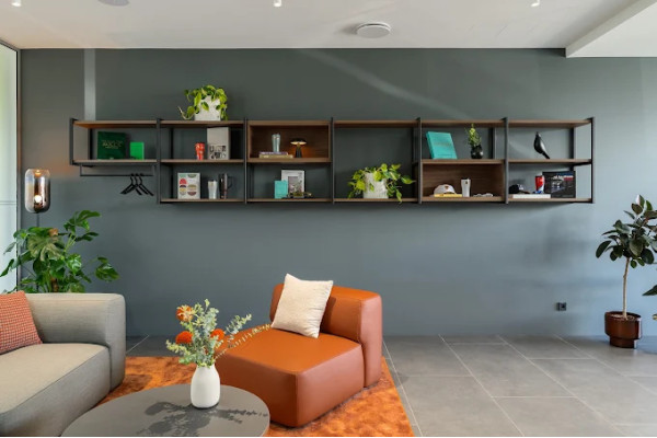 Relaxation area with orange chair, gray sofa and wooden wall shelves.