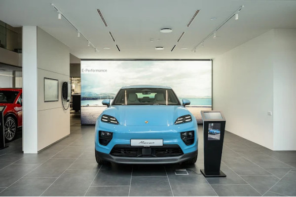Blue Porsche car in the exhibition area with light walls and ceiling lighting.