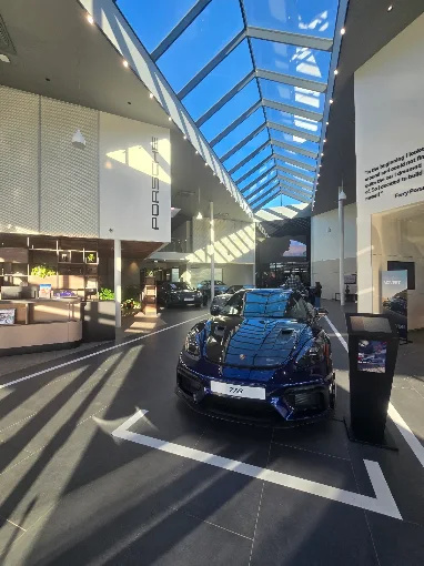 The high salon space of the Porsche Center with a glass roof and a car display.